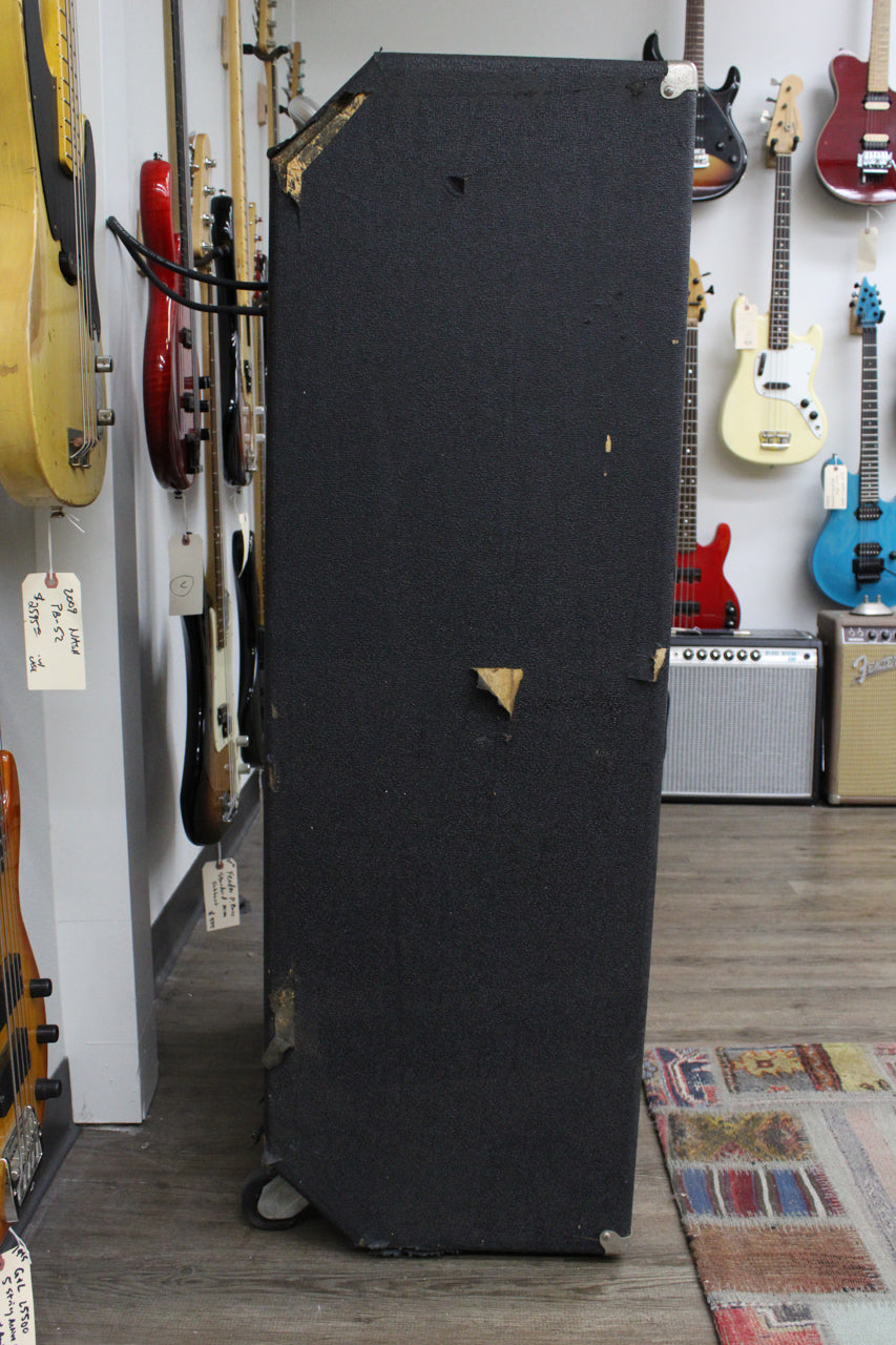 The tall, black textured speaker cabinet is shown from its right side, revealing scuffed corners, torn tolex, and two bottom casters.