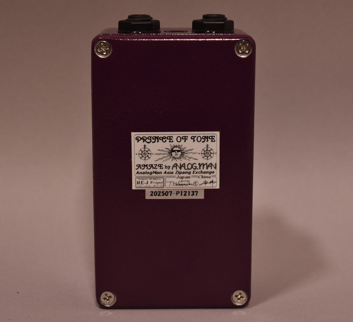 The purple pedal is viewed from the back, showing a white label with black text and four silver screws.
