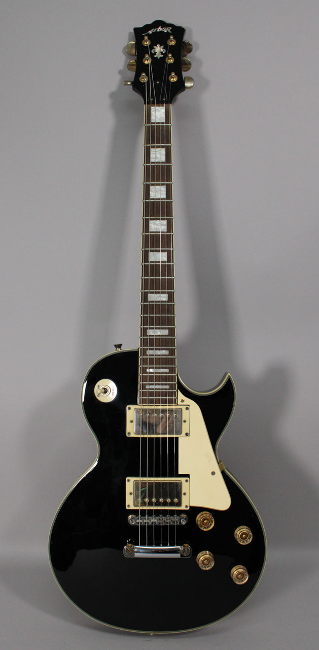 Full-length view of a black gloss Les Paul copy with cream pickguard, two humbuckers, four gold control knobs, and block inlays.