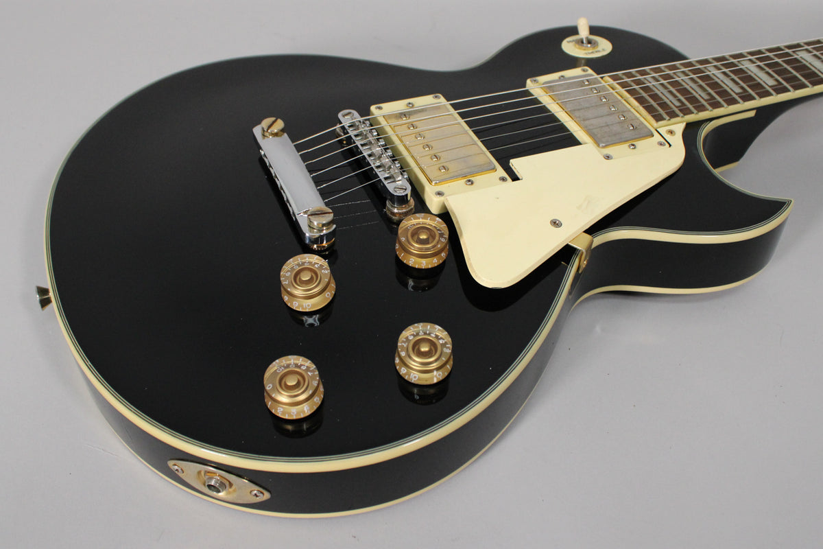 Close-up of a black gloss Les Paul copy, showing the lower bout, four gold speed knobs, cream pickguard, and two humbuckers.