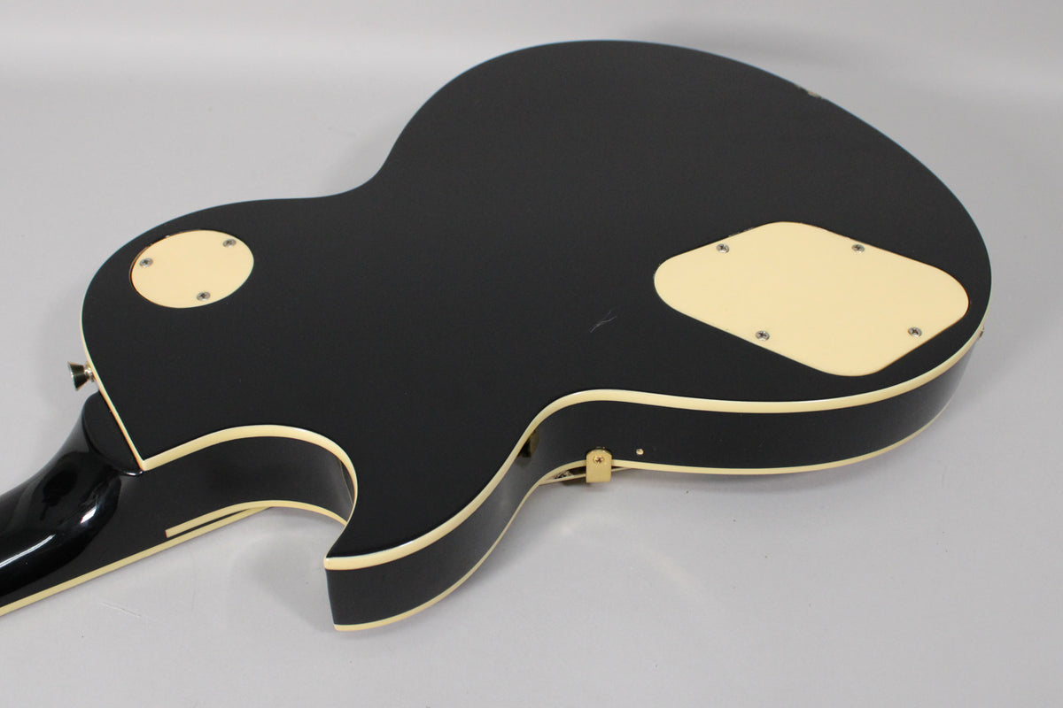 The guitar's black gloss back shows cream binding, two cream control cavity covers, and a small scratch near the upper cover.