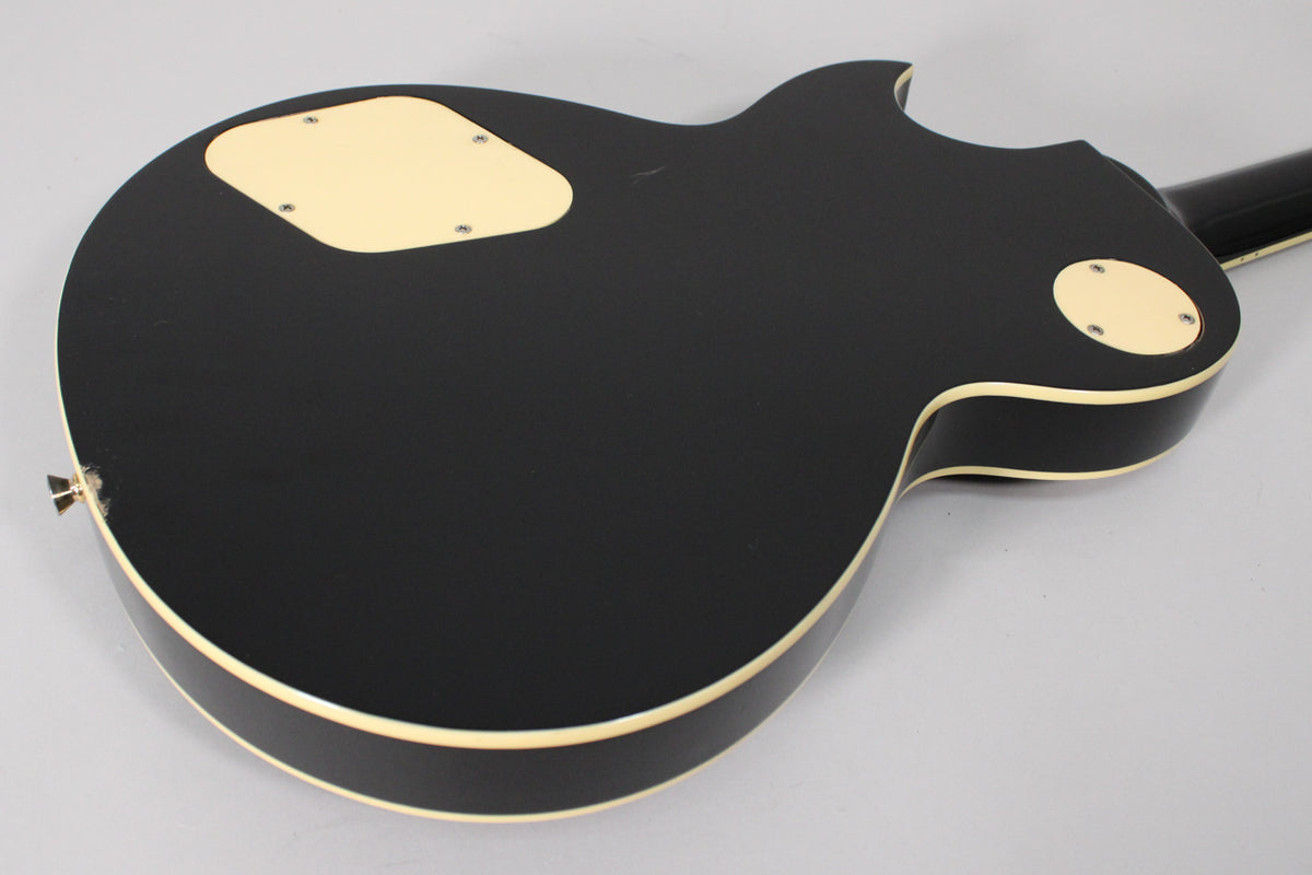 The guitar's black gloss back is angled, revealing cream binding, control cavity covers, and a chip near the strap button.