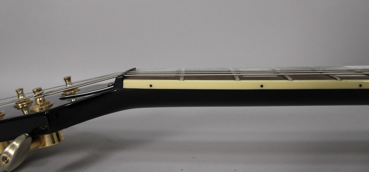 The black gloss headstock and neck, with gold tuners, are seen from the side, showing the cream binding and fretboard dots.