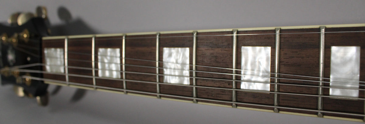 Close-up of the dark wood fretboard with rectangular mother-of-pearl inlays, cream binding, and silver frets and strings.