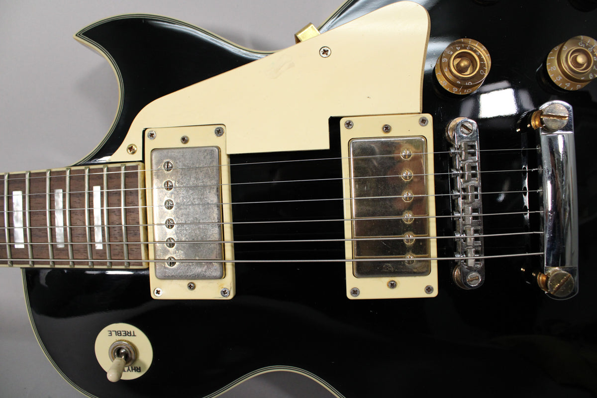 Close-up of the black gloss body with cream pickguard, two humbuckers, tune-o-matic bridge, and gold volume/tone knobs.