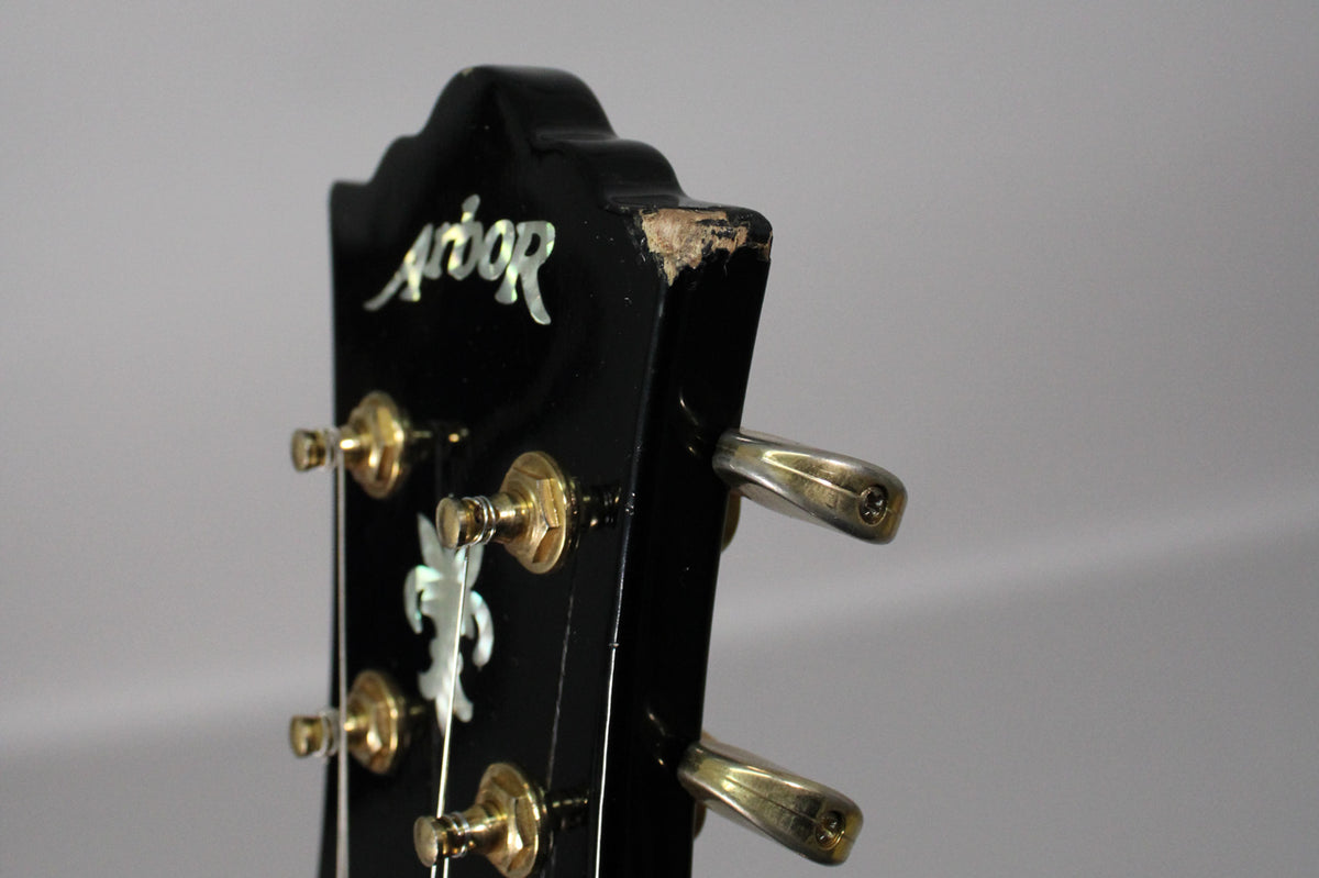 Close-up of the black gloss headstock with gold tuners and mother-of-pearl inlay, showing significant chipping on the top edge.