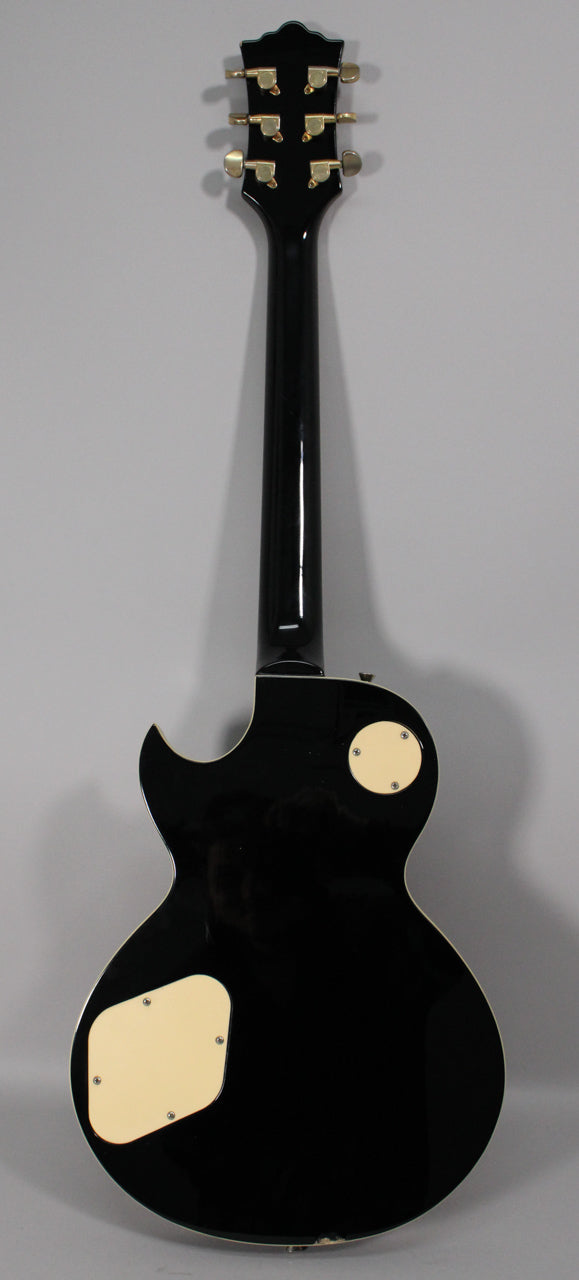 Full rear view of a black gloss guitar with cream binding, gold tuners, and two cream control cavity covers.