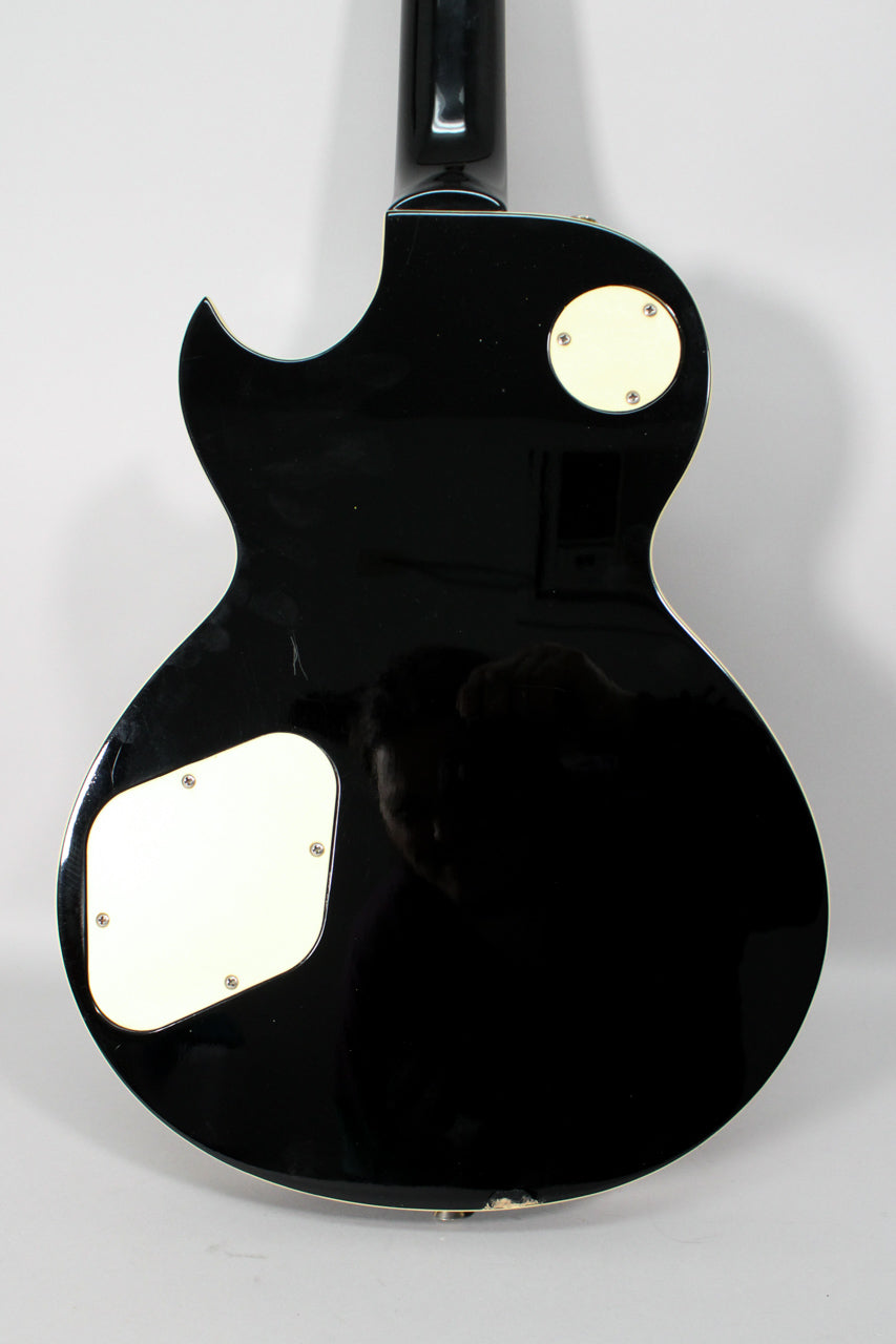 The guitar's black gloss back shows two cream control cavity covers and some wear, including a chip on the lower edge.