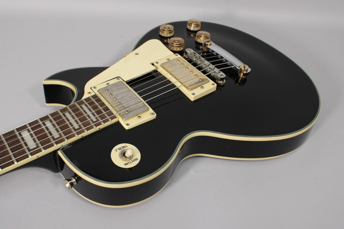 Black gloss electric guitar, angled view of the body and lower neck, showing cream binding, humbuckers, and gold hardware.