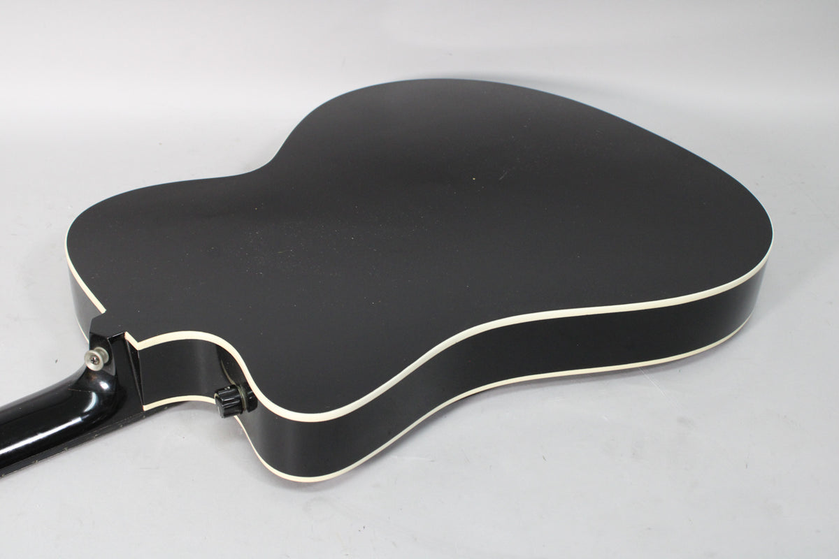The black thinline acoustic-electric guitar's back and sides are visible, with white binding and a black strap button.