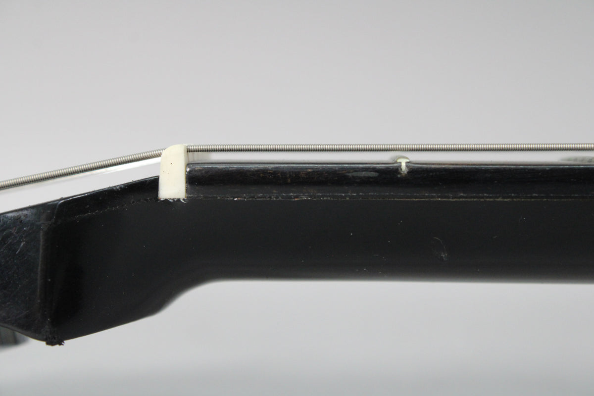 Close-up of the black gloss headstock and nut, showing a chipped nut and a small ding on the headstock face.