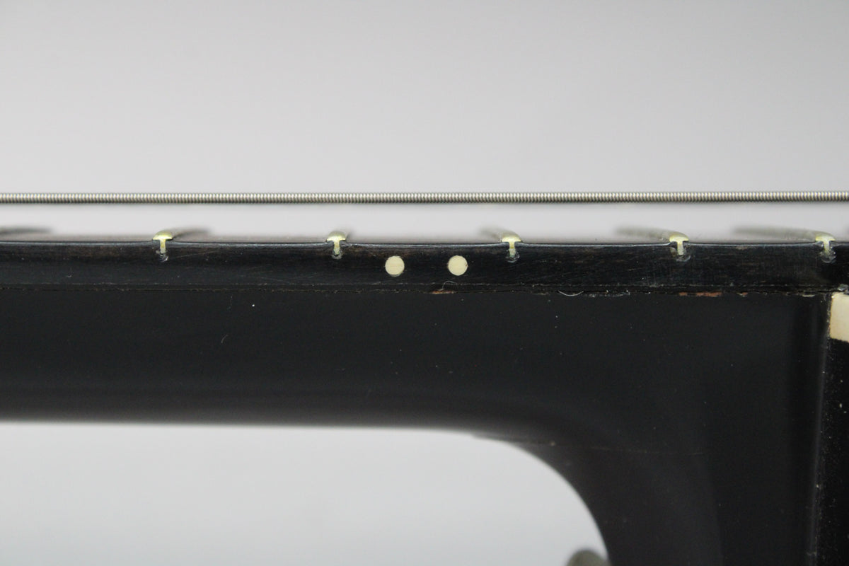Close-up of the black neck and fretboard, showing two light-colored side dot markers and some wear along the binding.