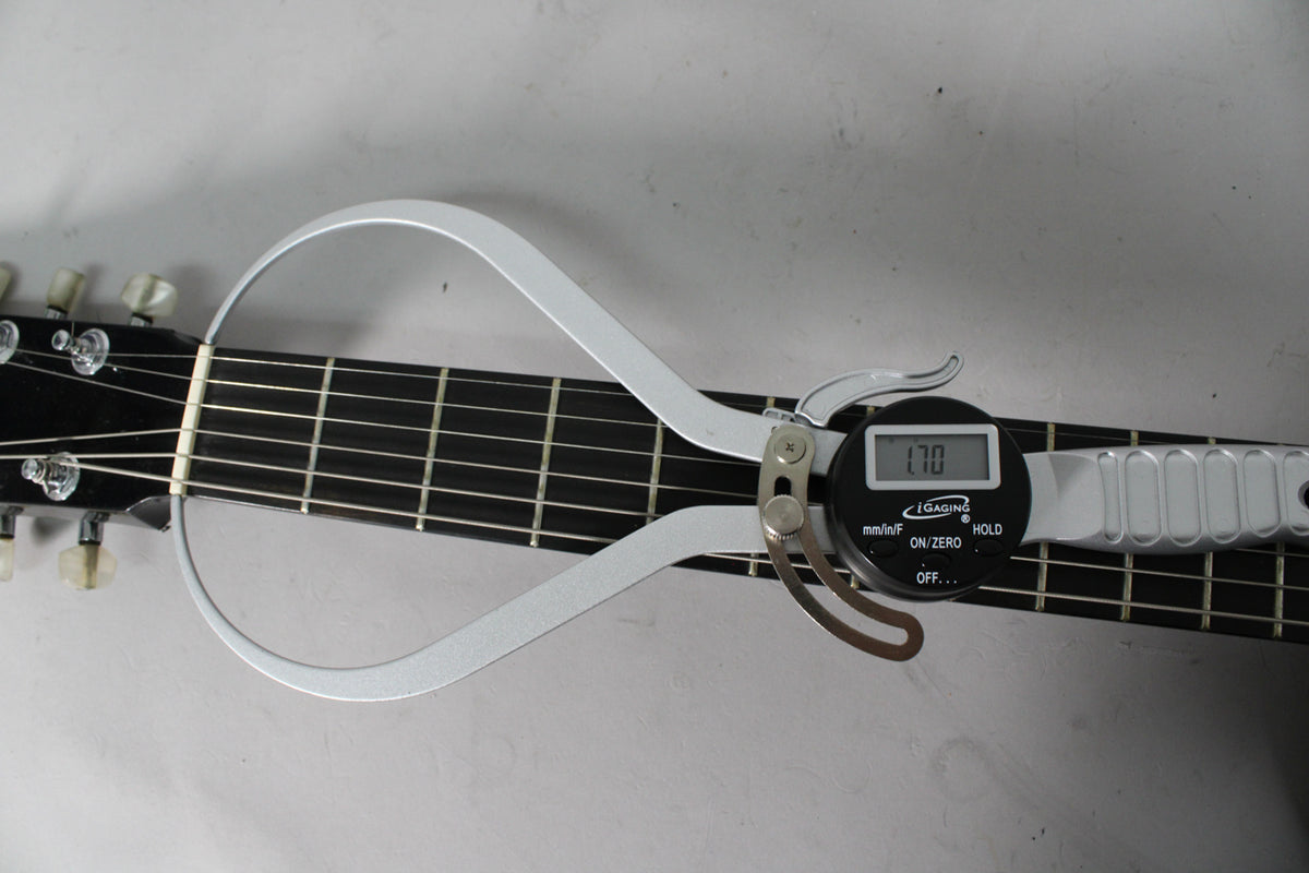 Overhead shot of the guitar's black fretboard and headstock, with a digital caliper measuring the nut width at 1.70 inches.
