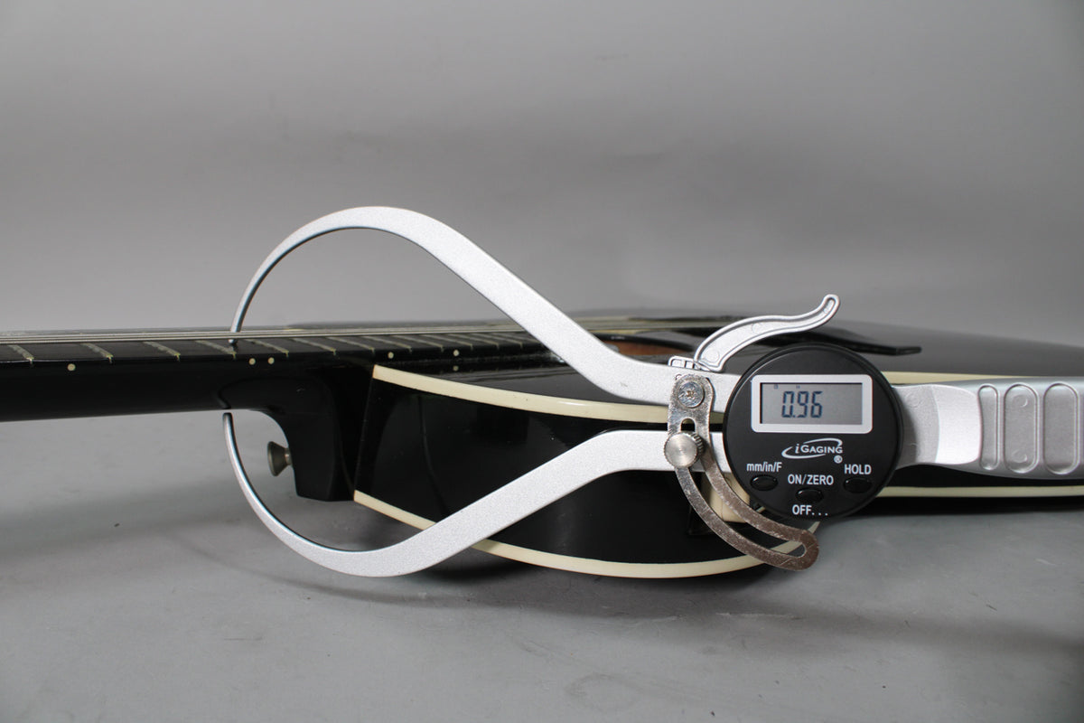 A digital caliper measures the black guitar's body thickness at the neck joint, displaying 0.96 inches.