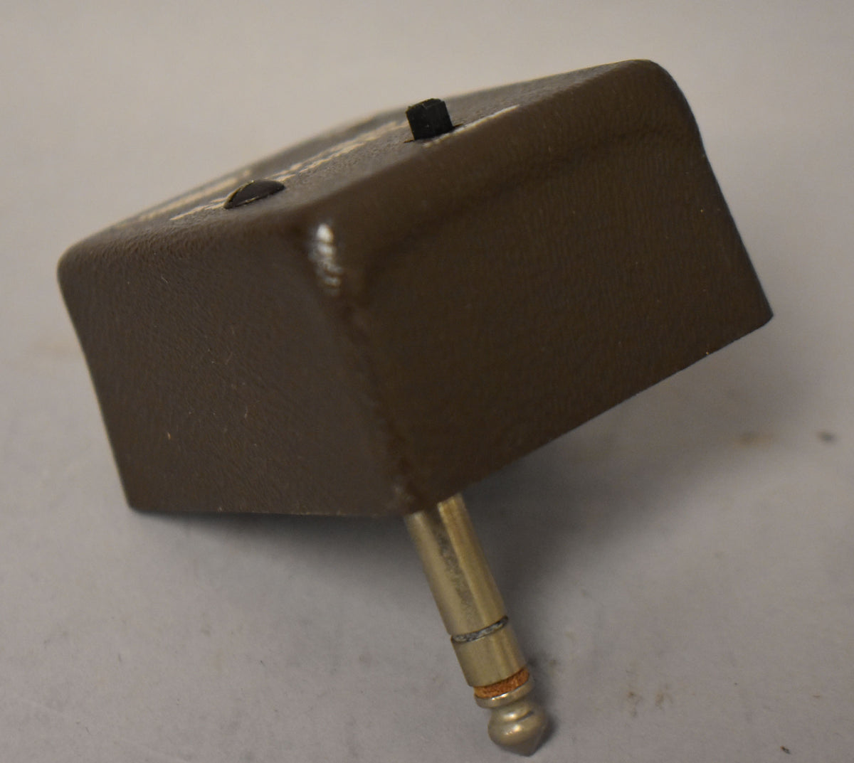 Dark brown textured box-shaped pedal with a brass 1/4-inch jack extending downwards, and two black knobs on top.