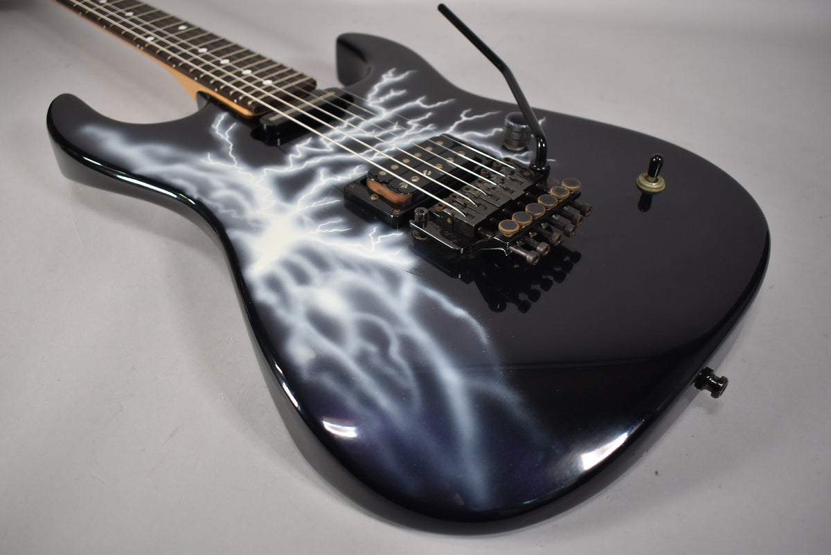 Black electric guitar with white lightning graphic, angled from the upper left, showing a black Floyd Rose tremolo and single toggle switch.