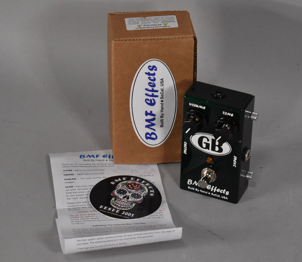 A dark green boost pedal with two black knobs, a footswitch, and an orange indicator light, next to its box and manual.