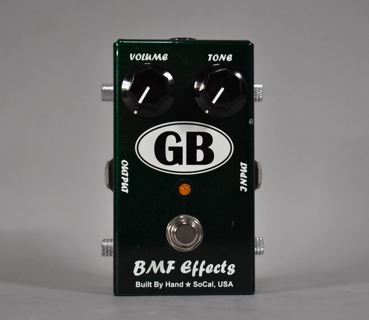 A dark green metallic guitar pedal, viewed from the front, with two black control knobs, a footswitch, and an orange LED.