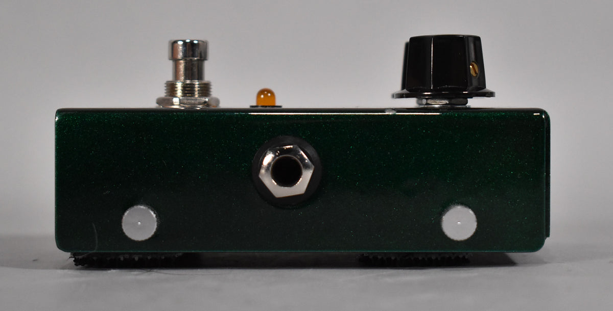 Side view of a dark green glitter guitar pedal with a black knob, amber LED, input jack, and two silver screws.