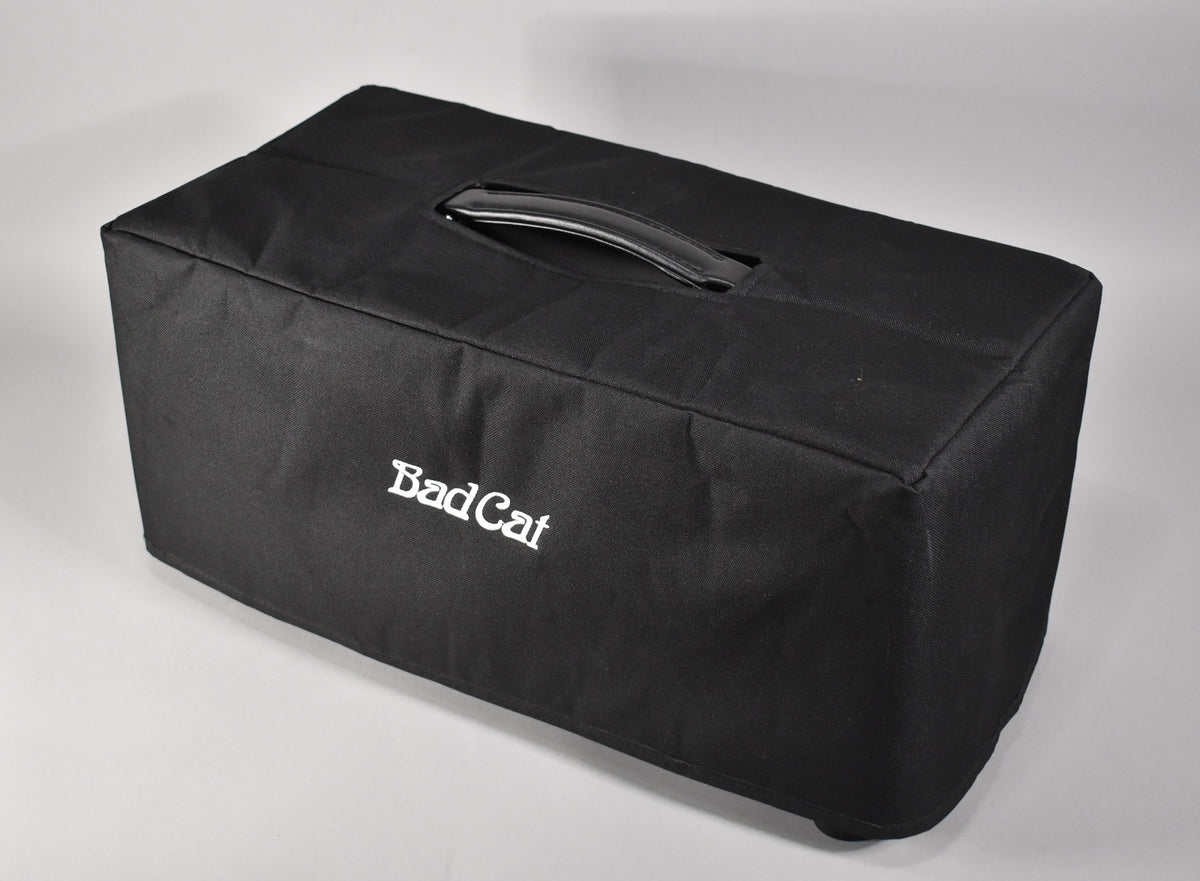 Black fabric cover for an amp head, seen from a high angle, with a black plastic handle on top and white embroidered lettering on the front.