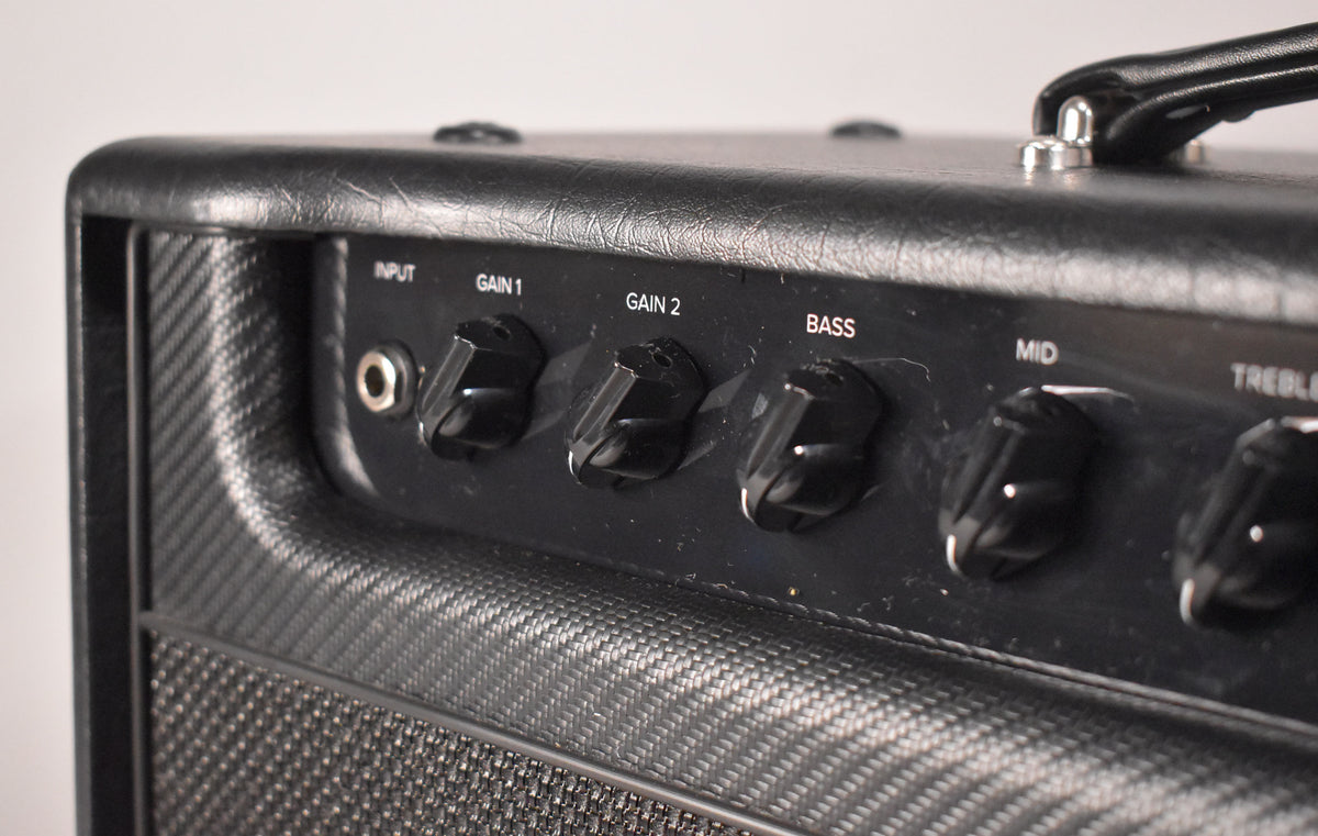 Close-up of a black guitar amplifier's control panel, showing Input, Gain 1, Gain 2, Bass, Mid, and Treble knobs.