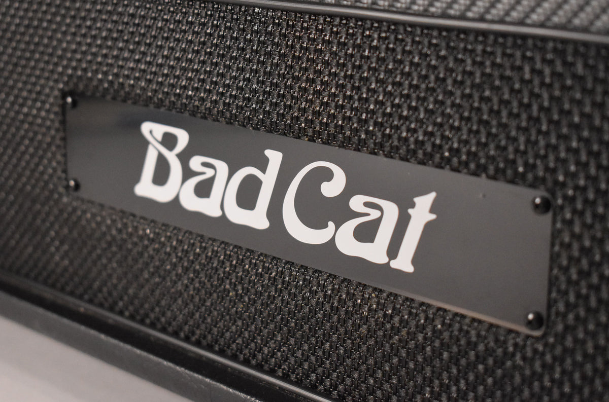 A close-up, angled view of the amp's black grille cloth, with a black rectangular logo plate featuring white lettering.