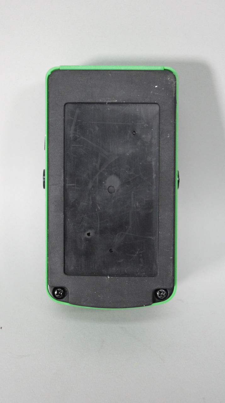 The pedal's underside is black plastic with a removable battery compartment, framed by a bright green metal casing with visible wear.