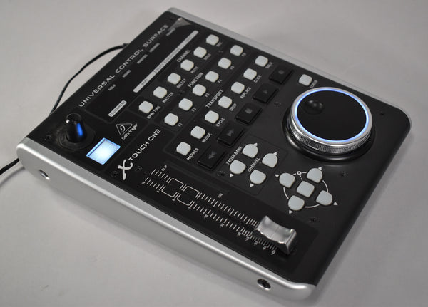 A black control surface with silver sides, featuring a large jog wheel, a single fader, and numerous white and black buttons.