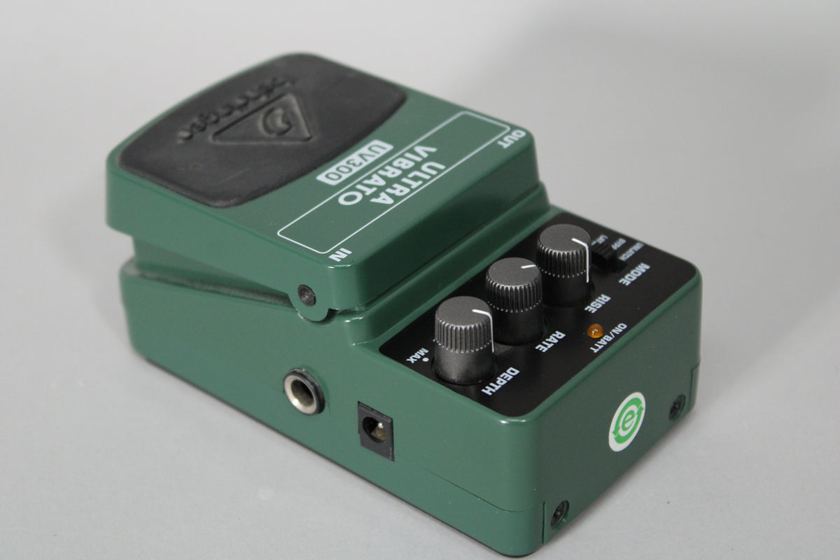 Dark green pedal with a black rubber footpad, three black knurled knobs, a small orange indicator light, and input/output jacks.