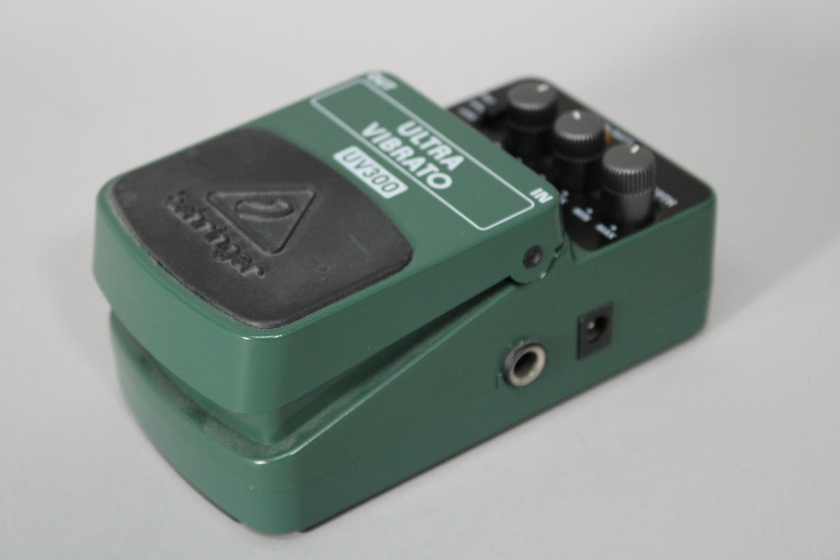 A dark green vibrato pedal, angled to show the black footswitch, three control knobs, and two input jacks.
