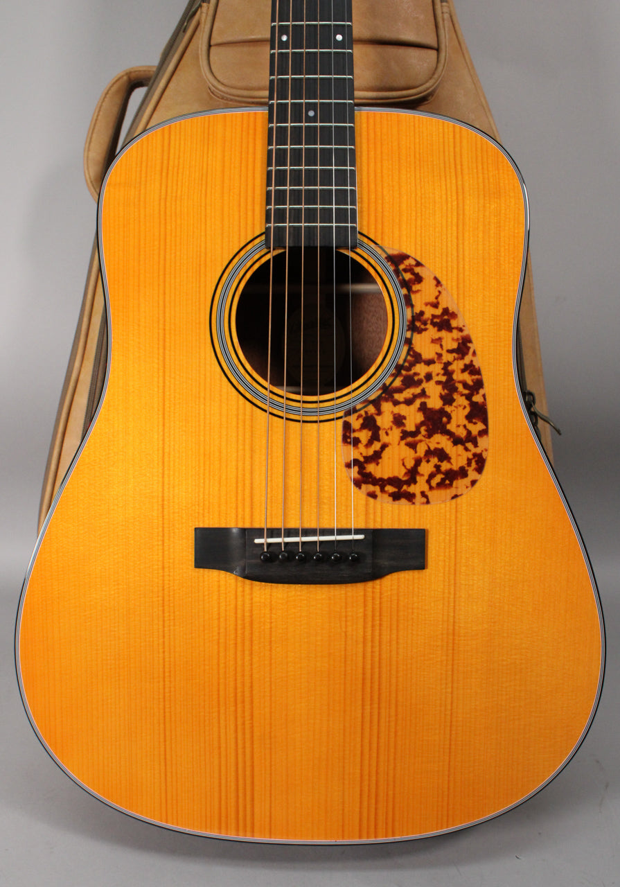 Full-front view of a light orange acoustic guitar with a tortoiseshell pickguard, black bridge, and dark fretboard.
