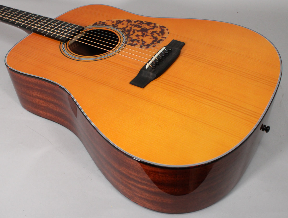 Angled view of a dreadnought acoustic guitar with a light amber top, dark mahogany sides, and a tortoiseshell pickguard.