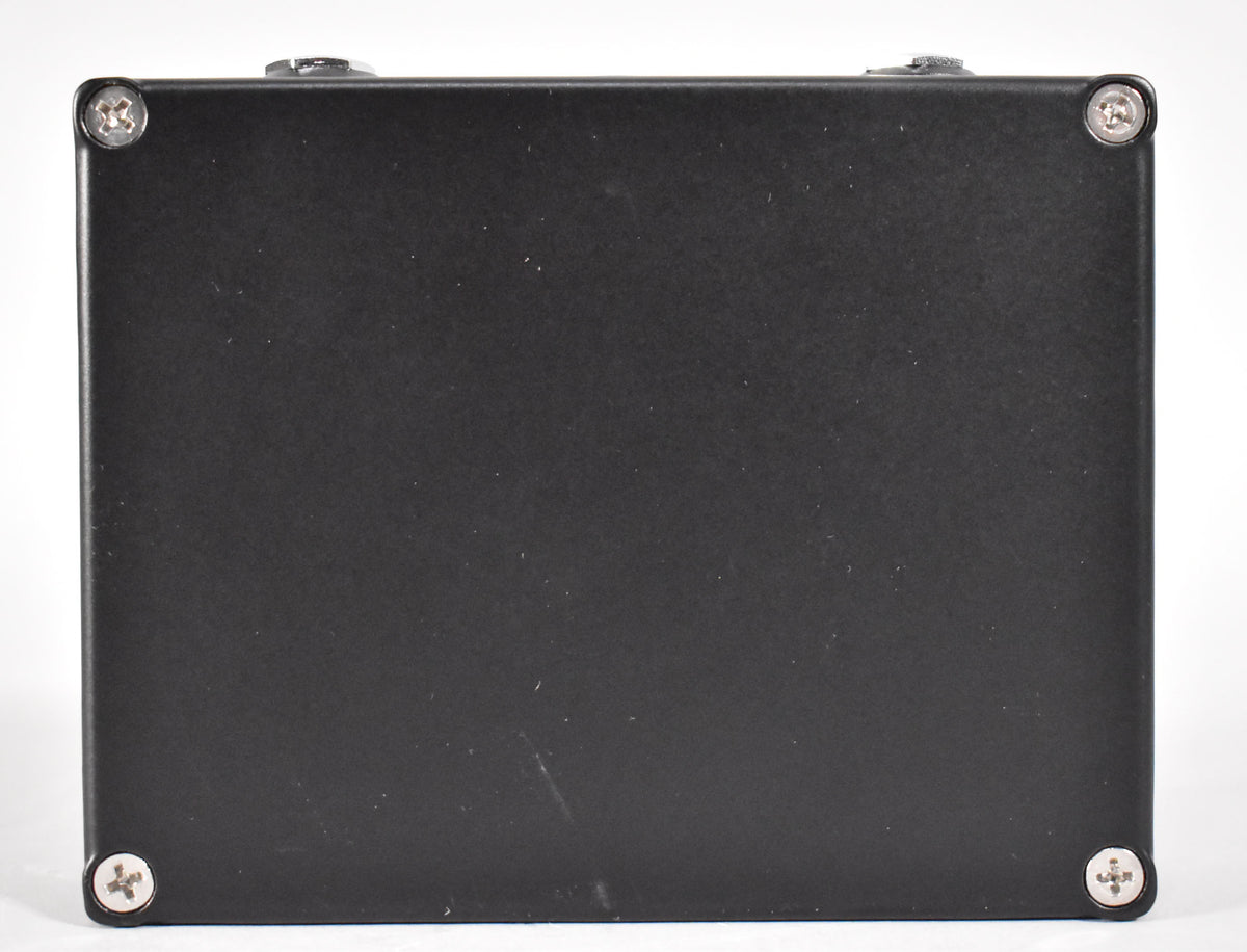 The black effect pedal is viewed from the bottom, showing four silver Phillips head screws in each corner.