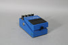 A blue effect pedal, viewed from the front-left, showing four black control knobs and a black rubber footpad with wear.