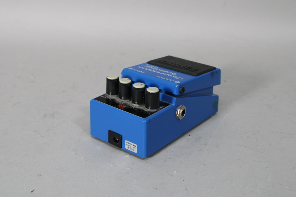 A blue effect pedal, angled to show the input/output jacks, four black control knobs, and a red indicator light.