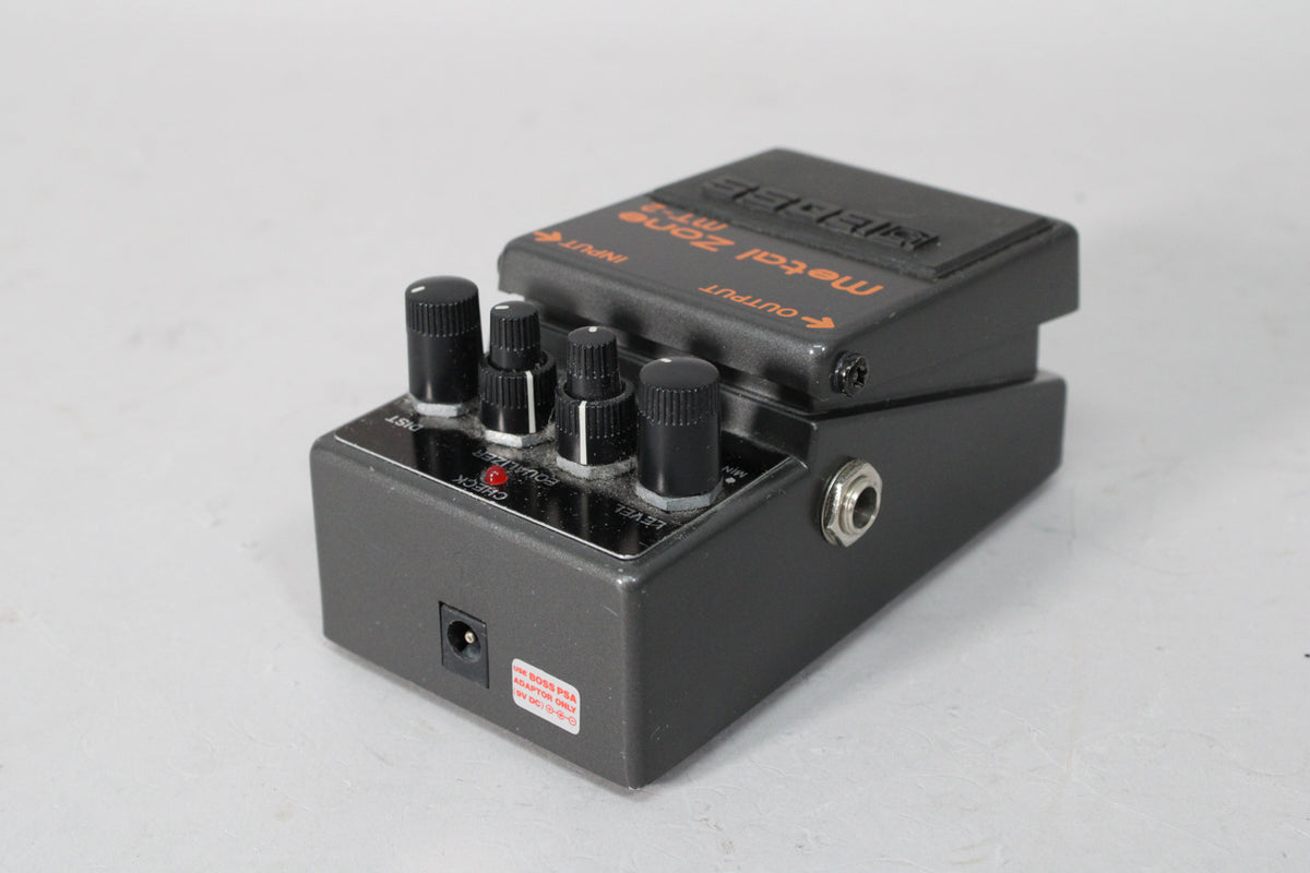 Dark gray pedal, angled from the right, showing four black control knobs, a red LED, and input/output jacks with some scuffs.
