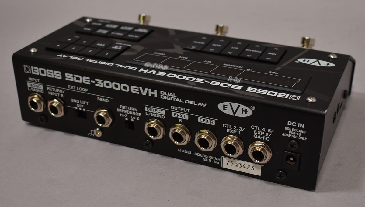 The black digital delay pedal is angled to show its rear panel with numerous silver input/output jacks and switches.