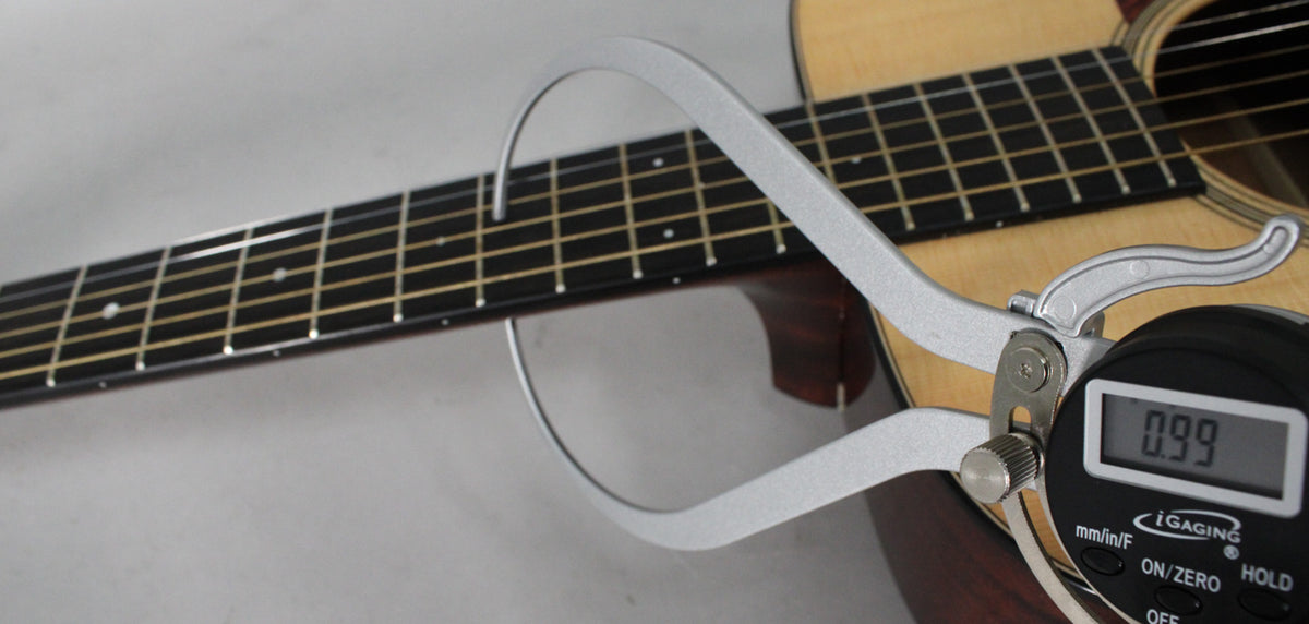 A digital caliper measures the string height at the 12th fret of the guitar's dark fretboard, displaying "0.99".