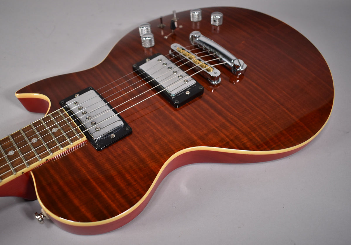 The guitar's cinnamon-flamed maple top with cream binding is visible from the lower bout to the neck joint, showing two chrome humbuckers.