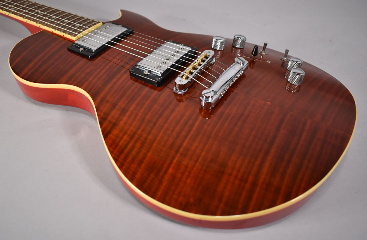 The upper body of a cinnamon-flamed guitar, showing chrome humbuckers, a tune-o-matic bridge, and four knurled chrome control knobs.