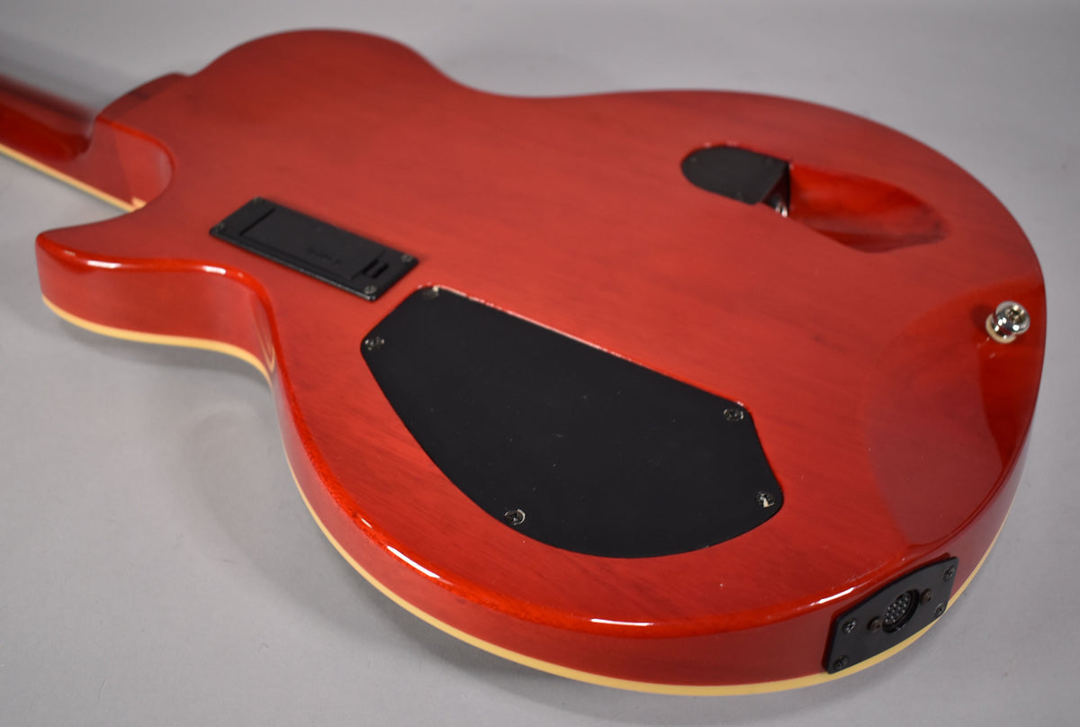 The back of a glossy red electric guitar with cream binding, showing black control cavity covers and a multi-pin output jack.