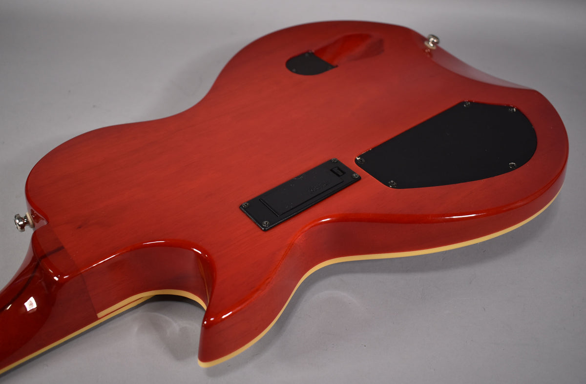 The back of a cinnamon-finished electric guitar, angled from the lower bout, showing black control and battery covers.