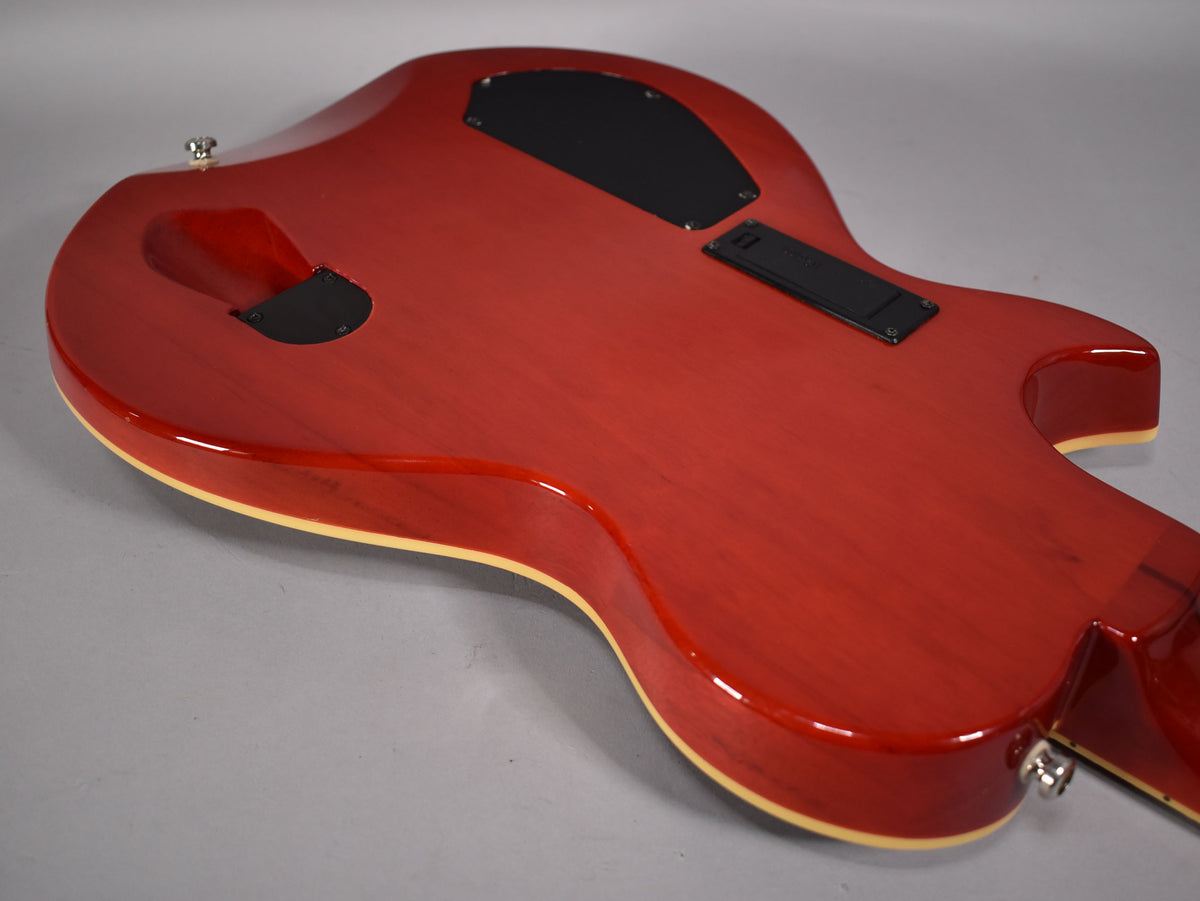 The back of a glossy cinnamon electric guitar, showing control cavity covers and a cream binding around the body.