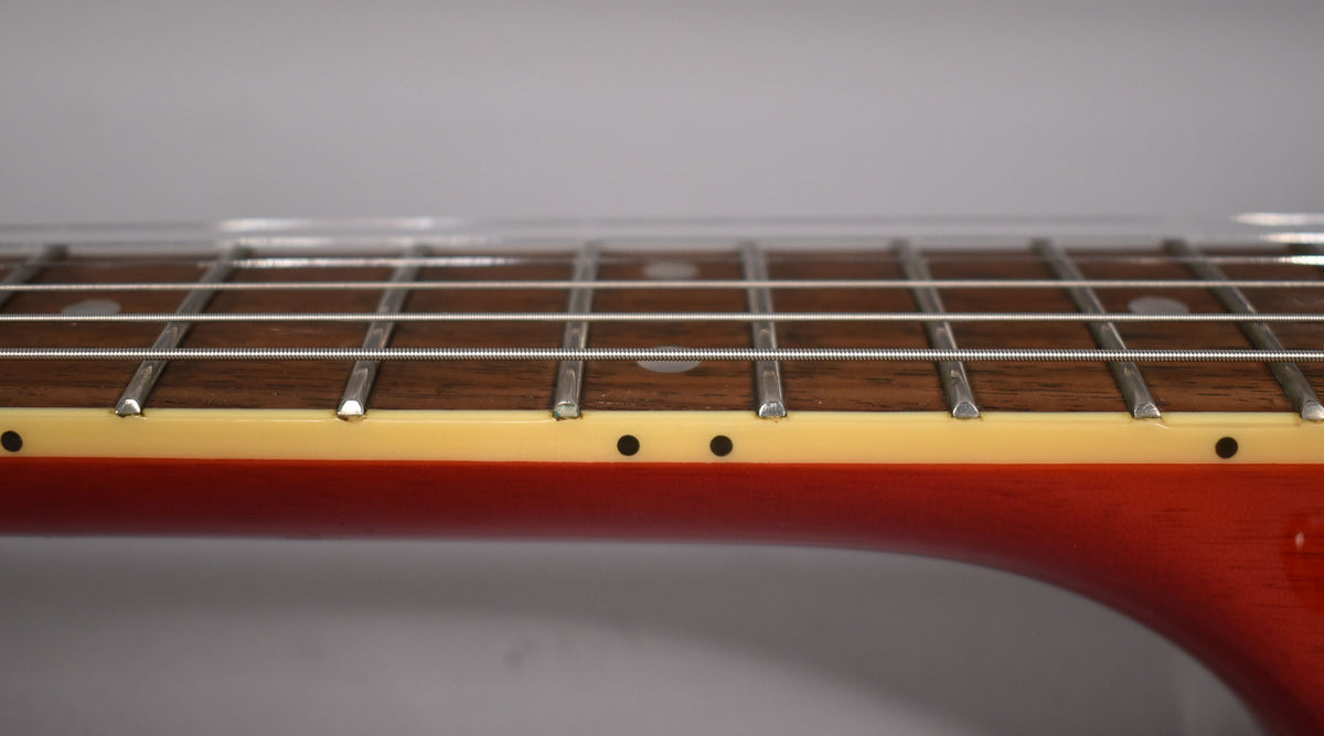 Close-up of the guitar's fretboard from the side, showing dark wood, metal frets, cream binding, and two black side dot markers.
