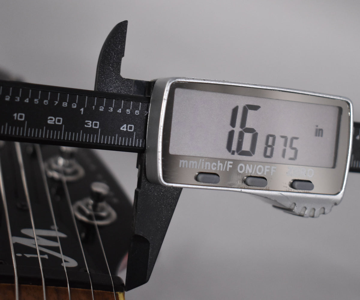 A digital caliper measures the guitar's nut width at 1.6875 inches, with the headstock and tuning pegs visible.