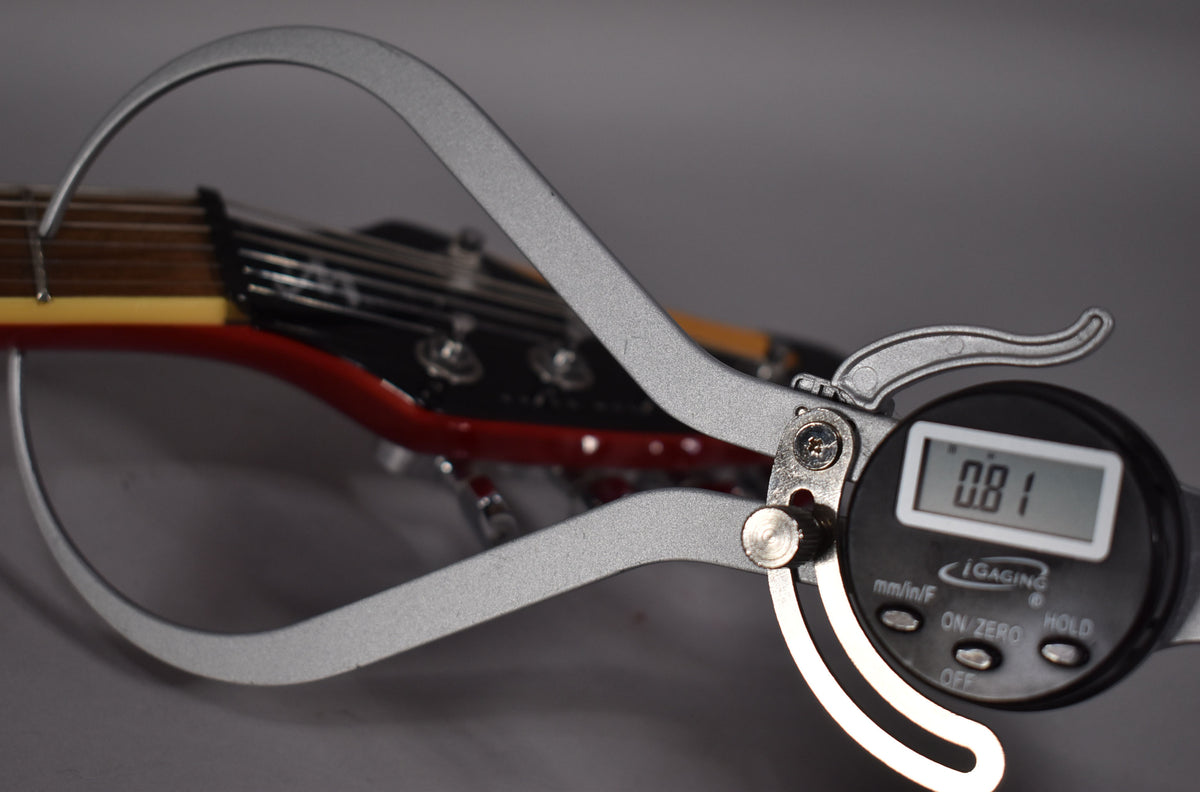 A digital string action gauge measures the guitar's strings at the nut, showing a reading of 0.81.