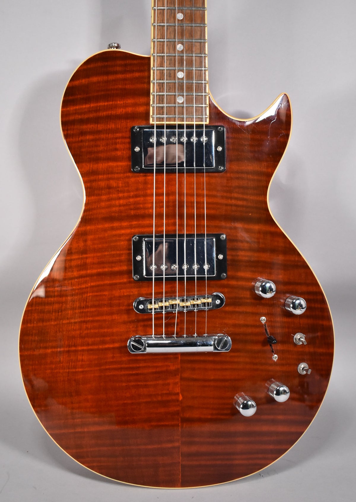 The guitar's cinnamon-flamed maple body is framed from the neck joint to the bottom, showing two humbuckers and four chrome knobs.