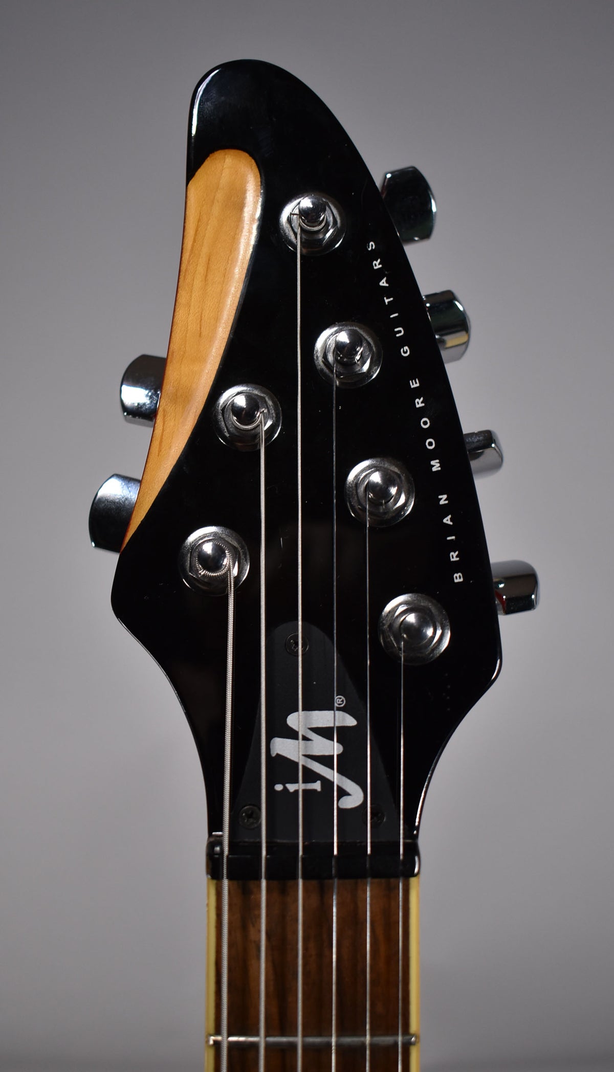 Close-up of the guitar's glossy black headstock with chrome tuners, a natural wood accent, and dark fretboard with light frets.