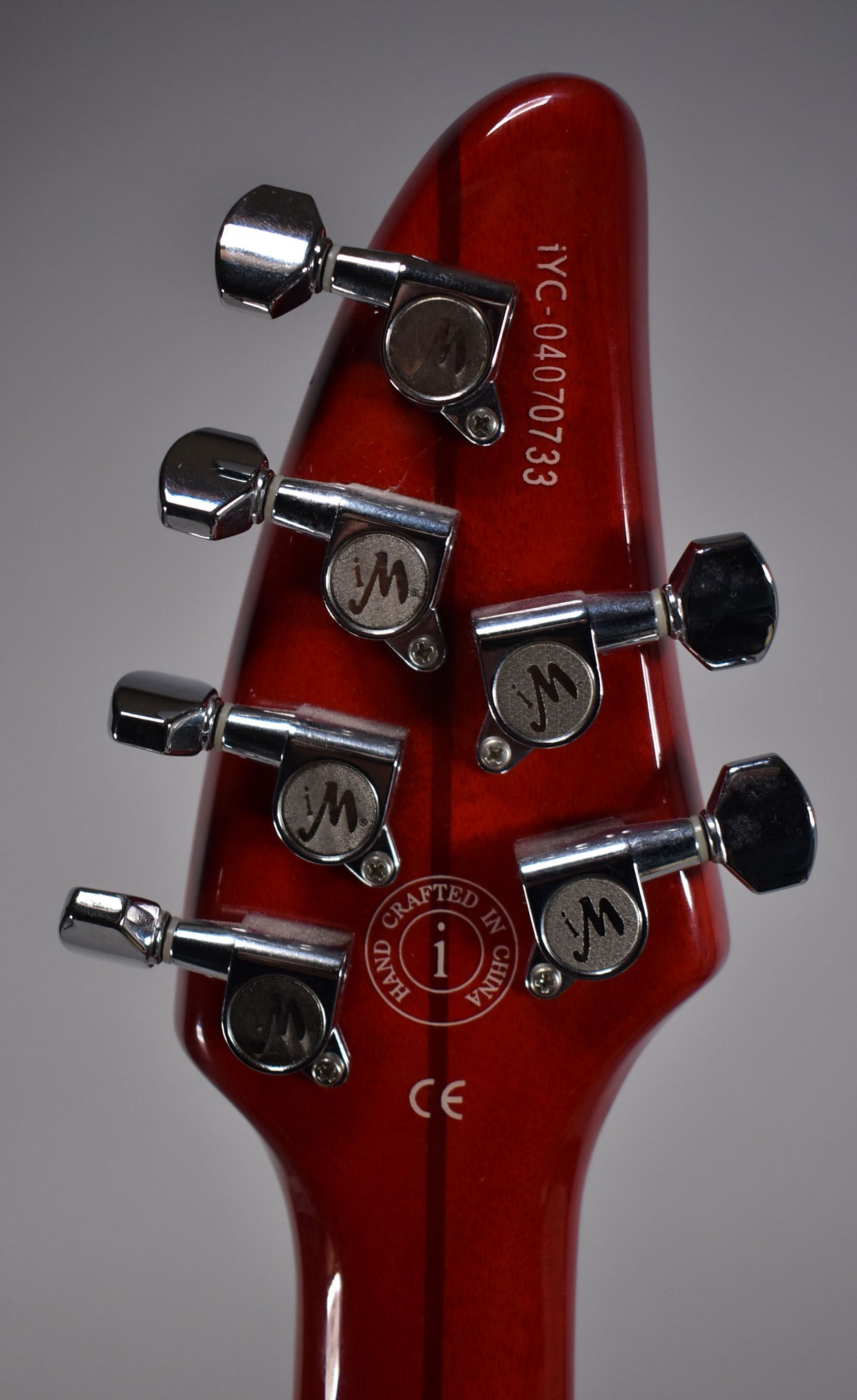 The back of a glossy cinnamon-finished headstock with six chrome tuners, showing some light surface scratches.