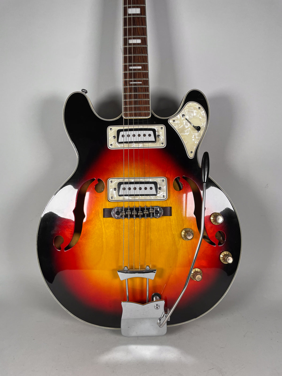 Front view of a sunburst hollowbody electric guitar with f-holes, two white-framed pickups, a pearloid pickguard, and a tremolo arm.